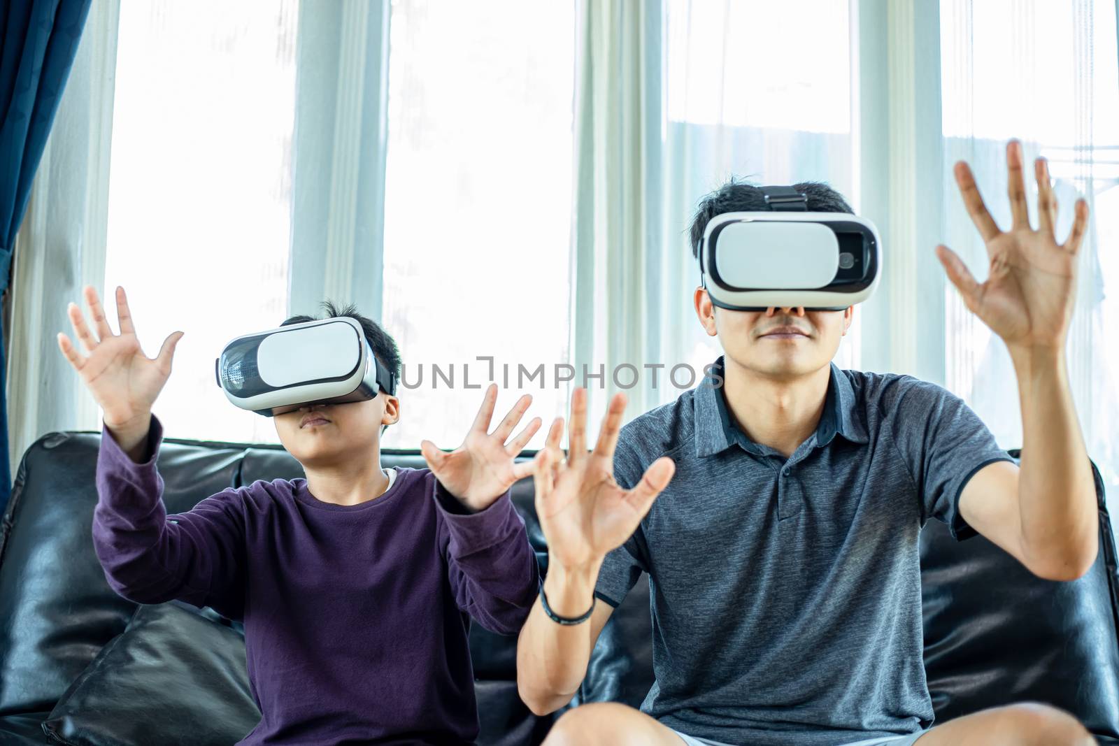 Asian father and son enjoy playing video games together with video joystick and Virtual Reality Glasses with exciting and very fun in the living room at home