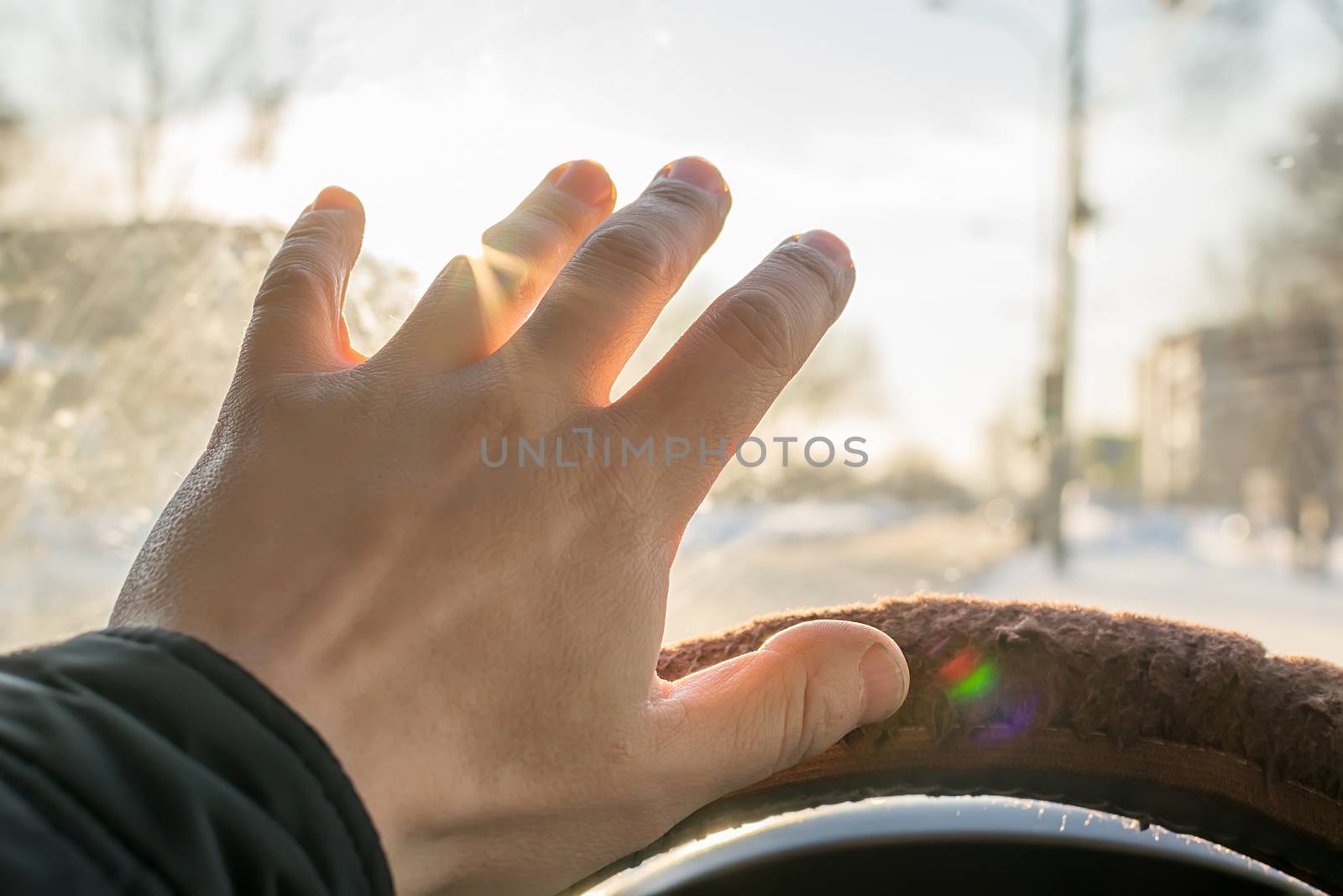 The hand of the driver of the car covers the sunlight, which blinds the person to see the road situation