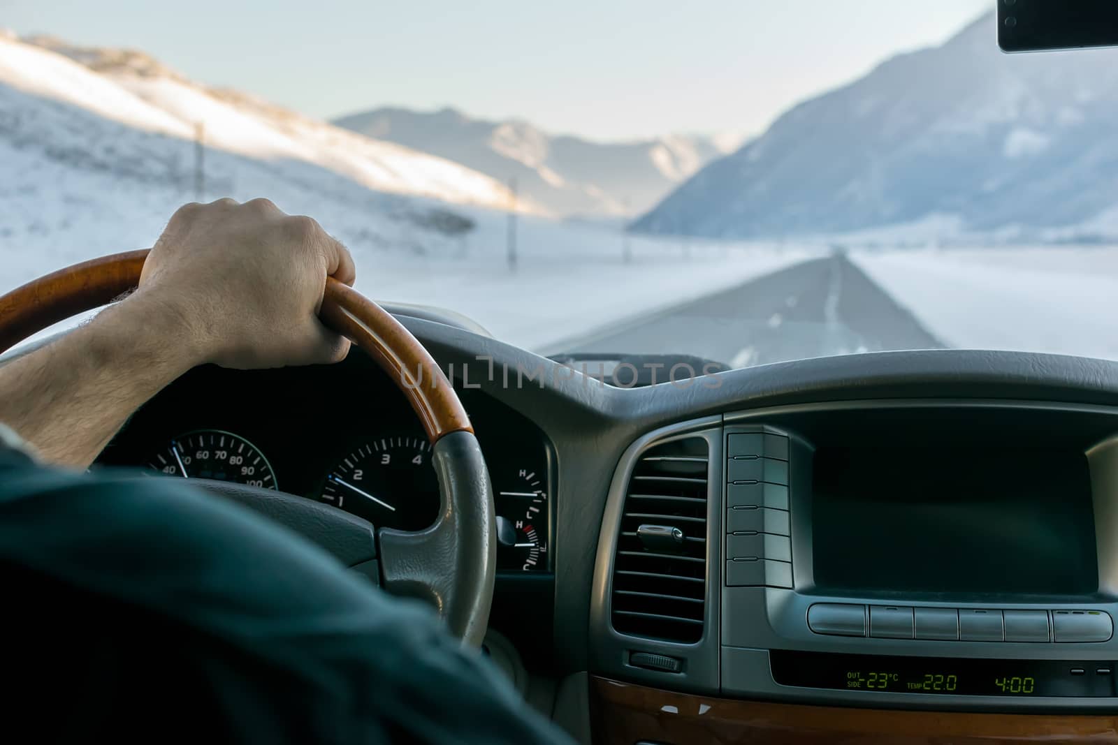 Close-up of a man's hand on the steering wheel of a car that moves on a snowy road among the mountains in the winter