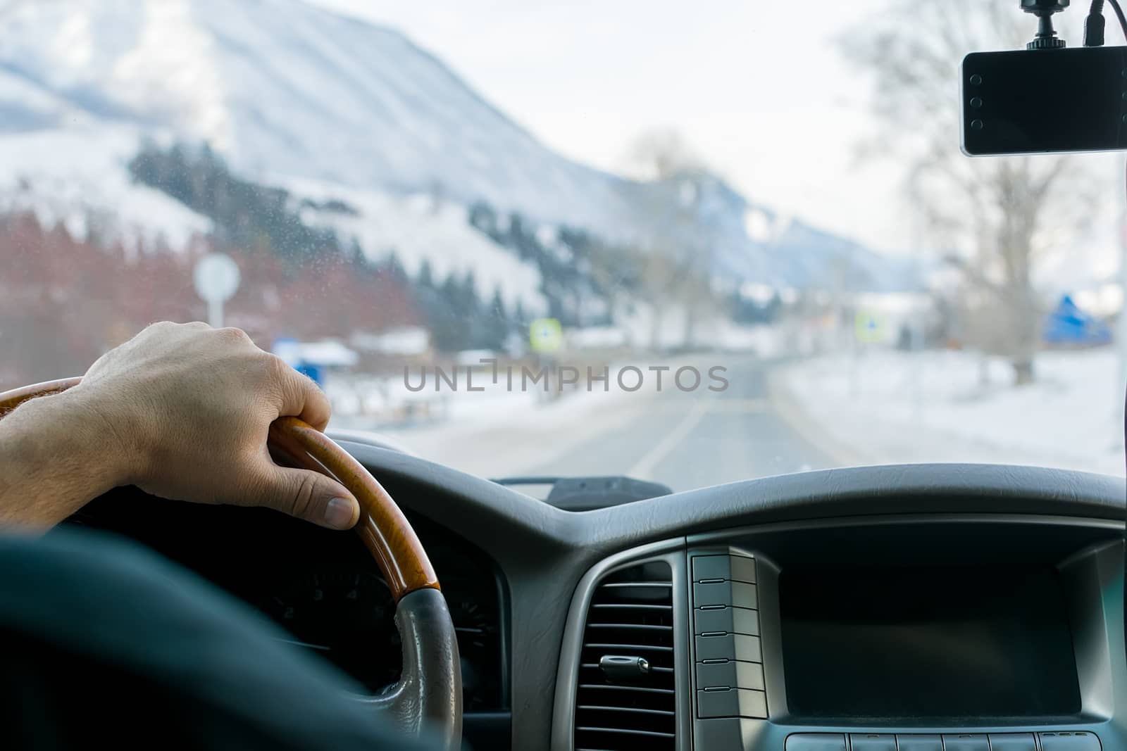 Close-up of a man's hand on the steering wheel of a car that moves on a snowy road among the mountains in the winter