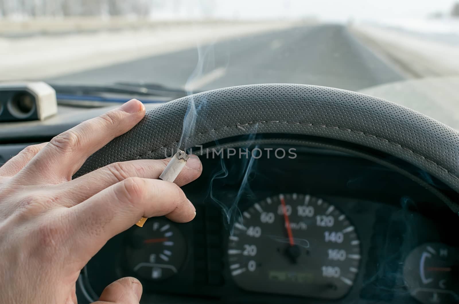 a Smoking cigarette in the hand of a Smoking car driver while driving on a snowy highway against the background of the speedometer on the dashboard