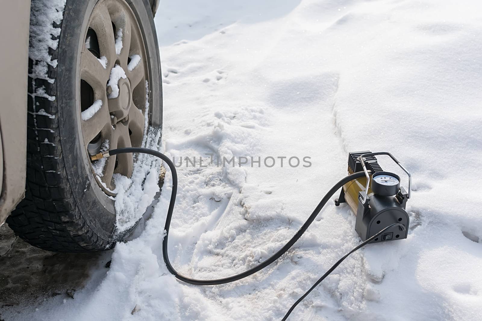 pump, automobile compressor for inflating tires with air stands in the winter on the snow and pumps the flat tire of the car