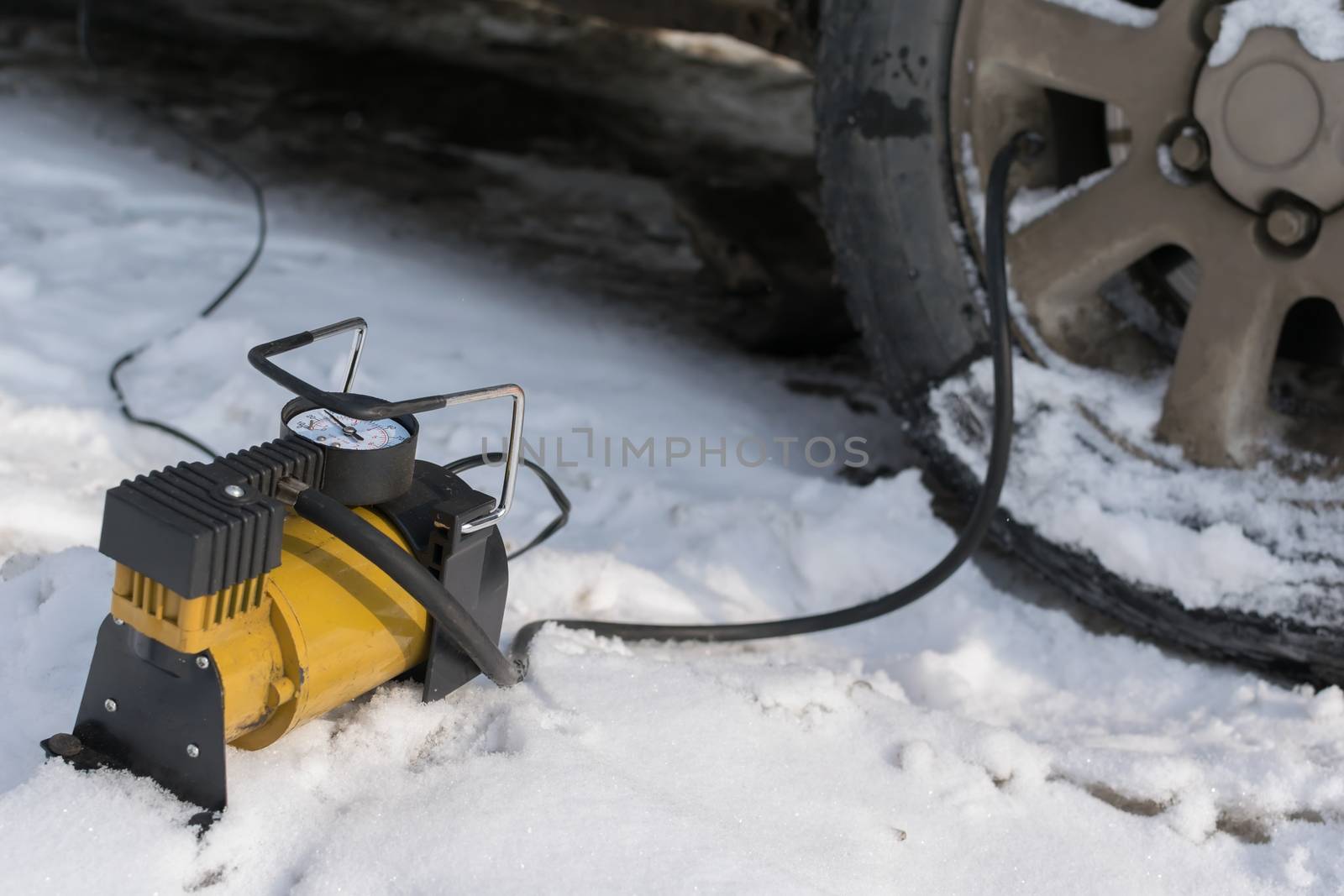 pump, automobile compressor for inflating tires with air stands in the winter on the snow and pumps the flat tire of the car
