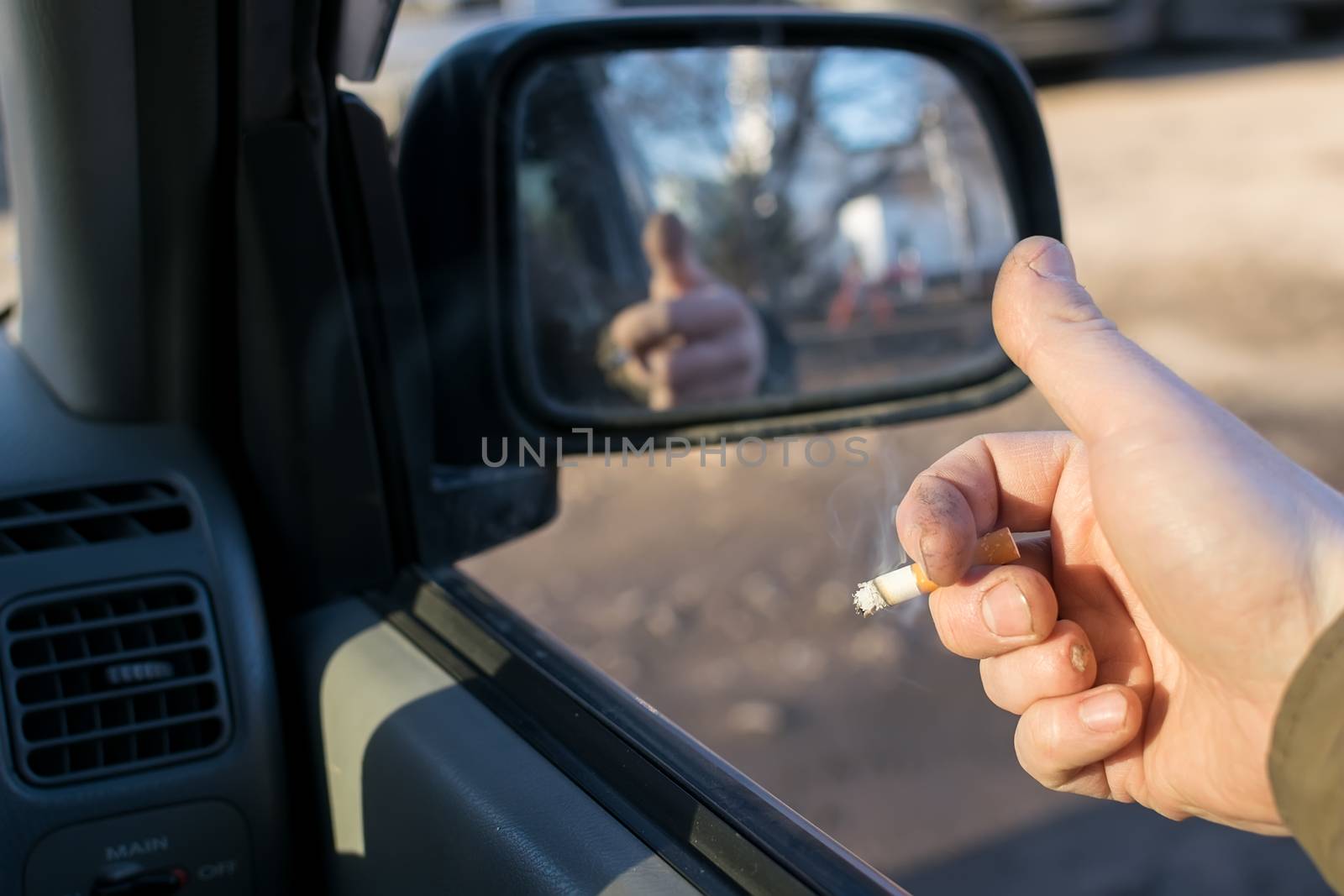 closeup of male hand with the missing finger holding a cigarette in a car in a residential area