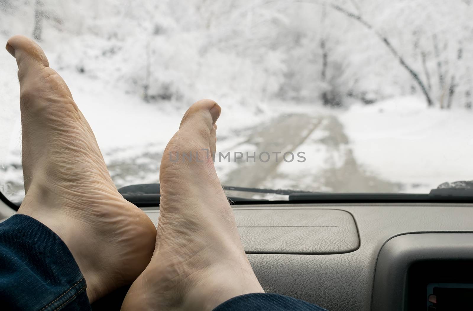 bare human feet on the windshield panel of the car on the background of snowy forest landscape and road