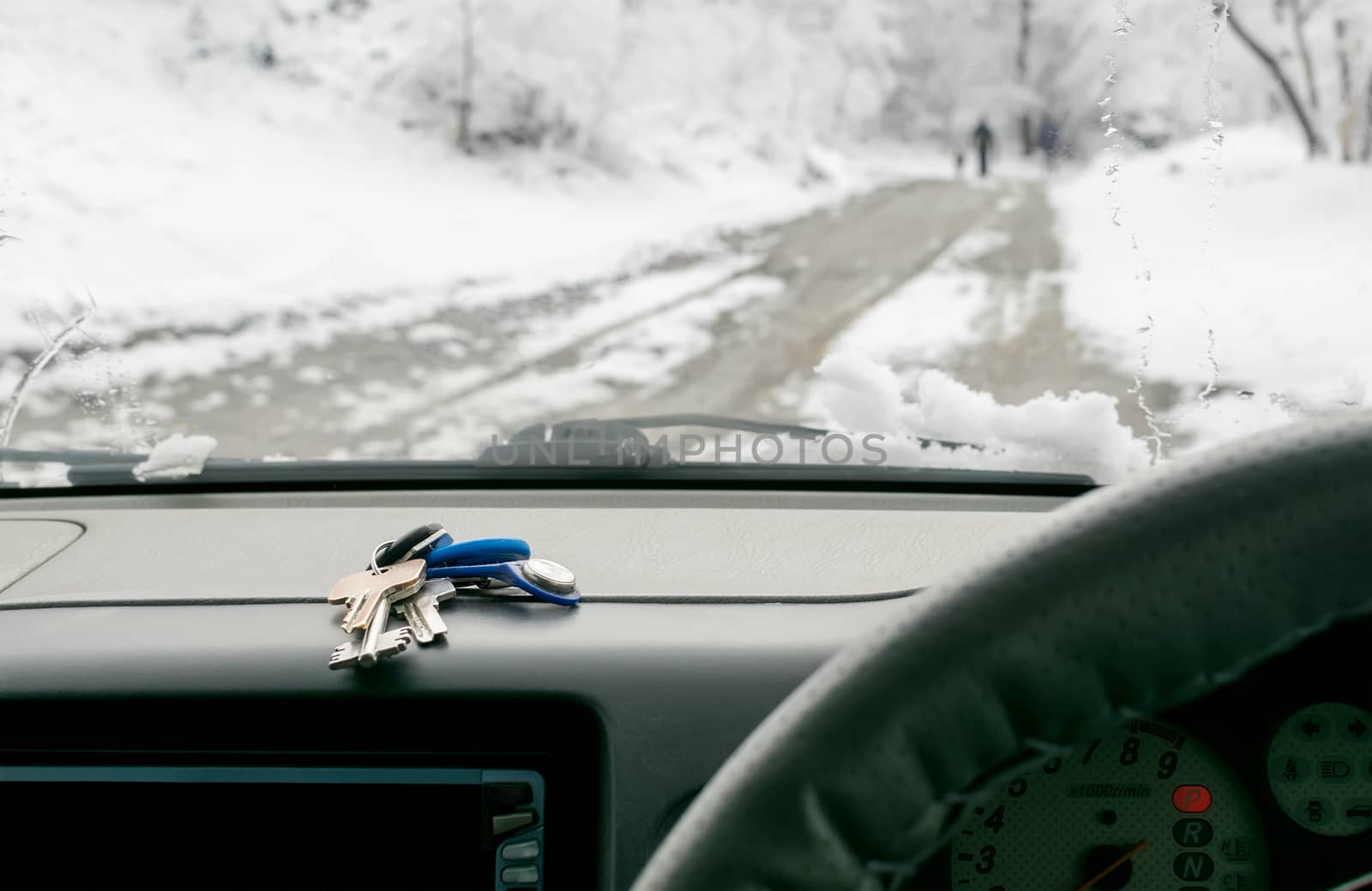 a bunch of keys lies on the dashboard of the car on the background of walking people on a wet snow-covered road outside the window in the winter