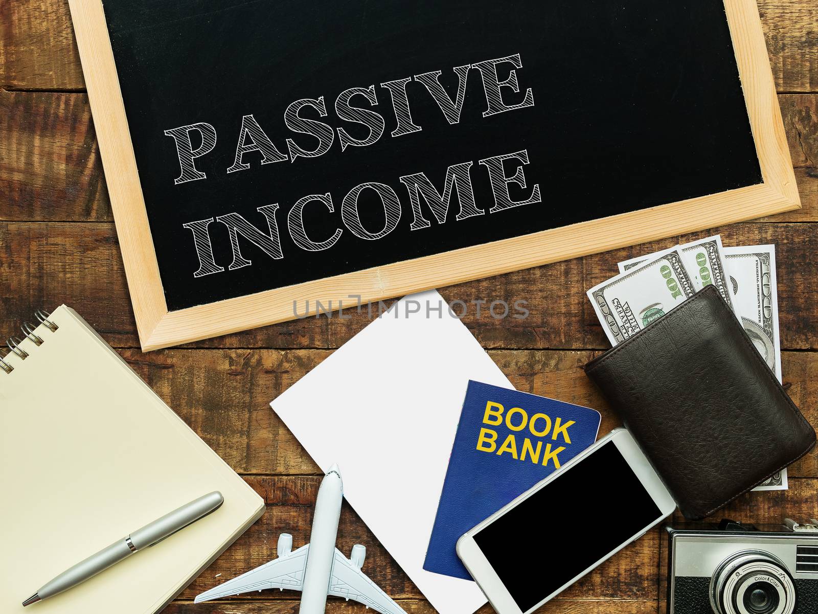 passive income, financial concept. text PASSIVE INCOME on chalkboard at the wooden table with book bank , money wallet , banknote , mobile phone , plane model and camera