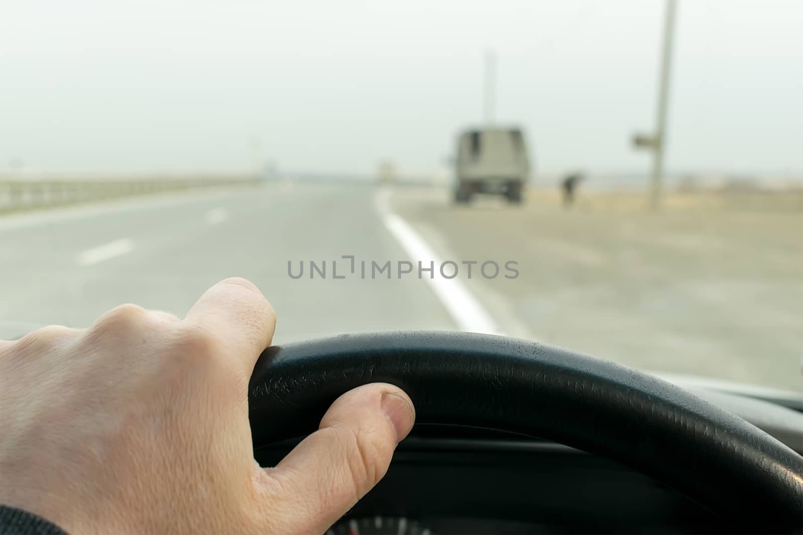View of driver's hands on the wheel of a car that travels on the highway near parked on the side of the truck