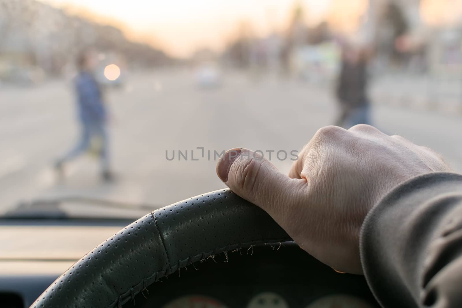 view from the car, the man's hand on the steering wheel of the car, located opposite the pedestrian crossing and pedestrians crossing the road