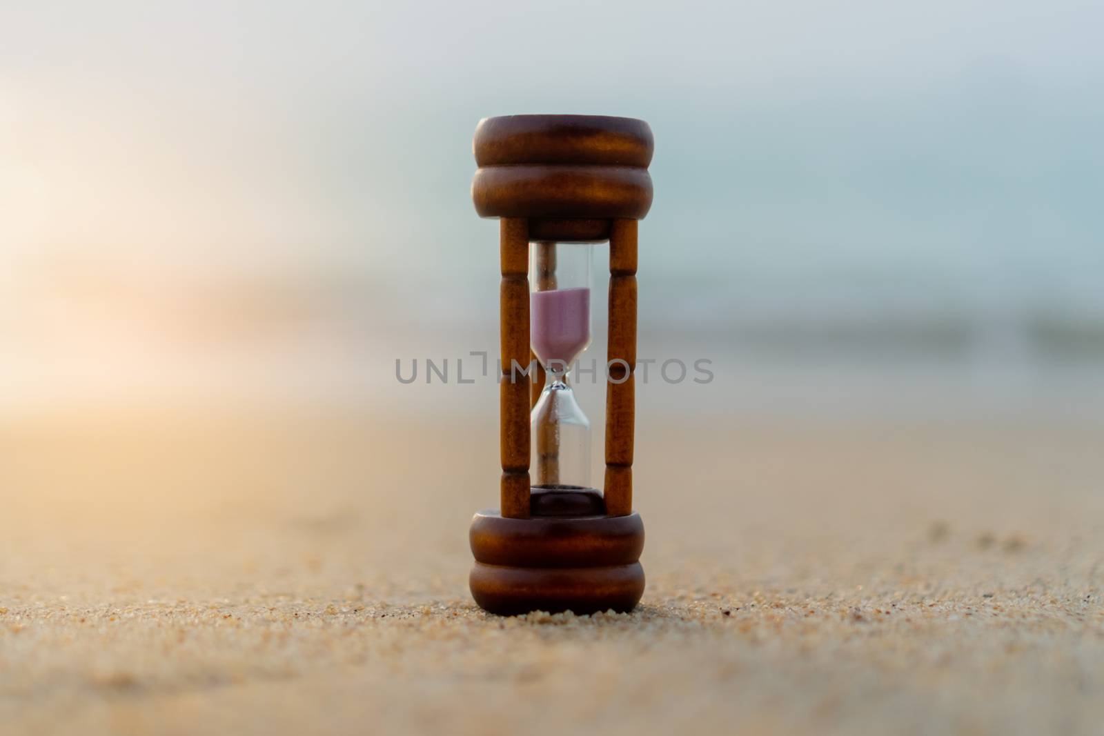 Small hourglass show time is flowing on sand beach background. by Suwant