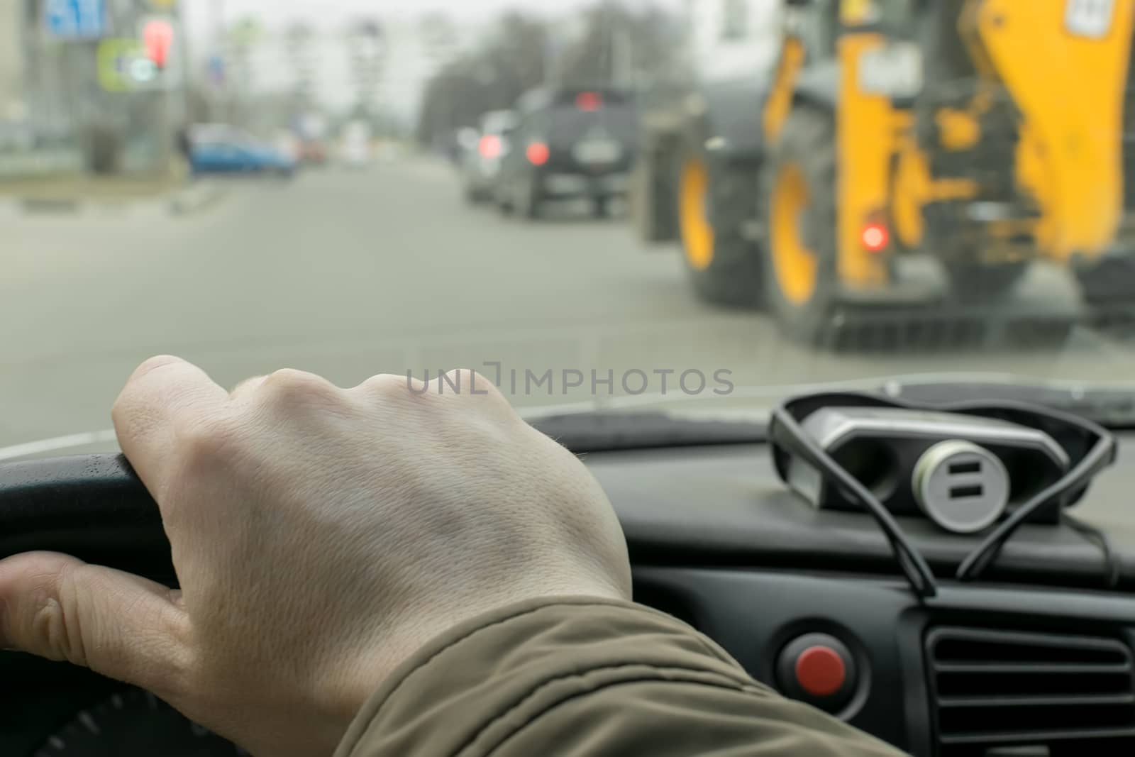 View of the driver's hand on the steering wheel of a car that rides on a city road on the background of a passing tractor nearby