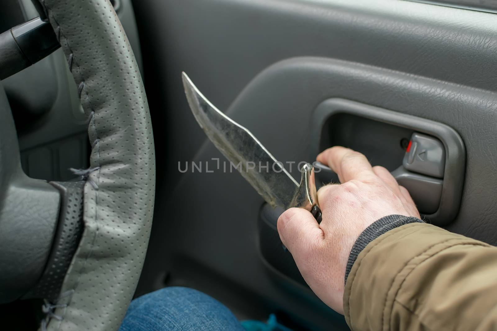 View of the knife in the hand of the driver inside the car, which is going to open the door