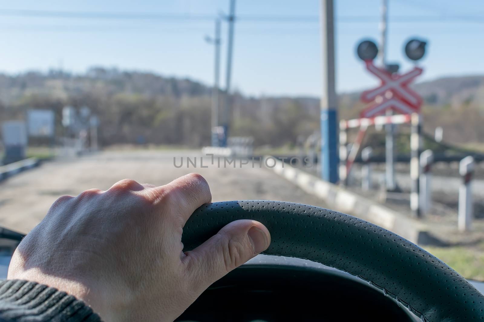 View of the driver's hand on the steering wheel of the car, which stopped before the railway crossing and indicator road signs