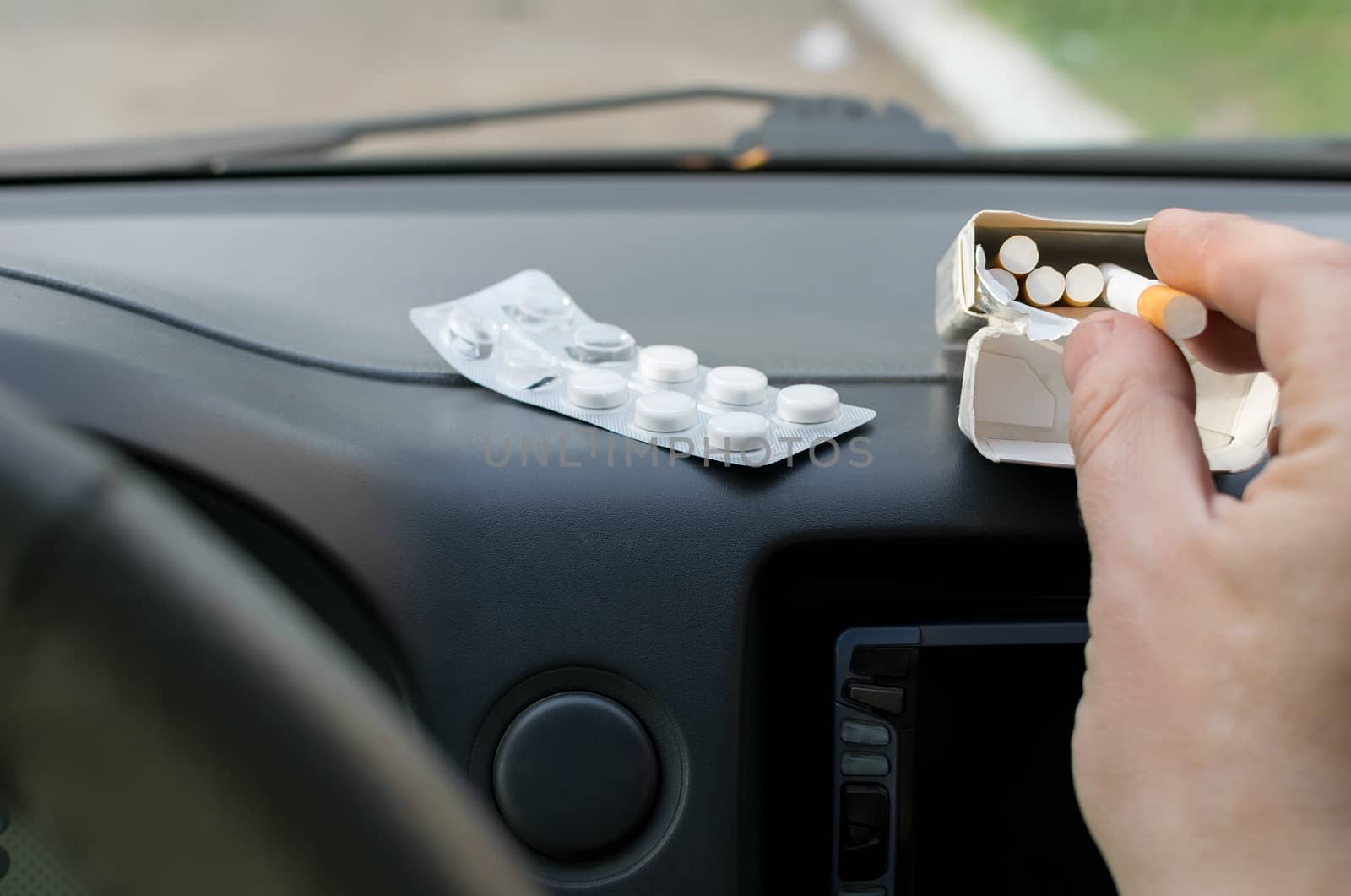 the hand of the person, the driver, takes a cigarette from the panel of the car with the package of tablets lying nearby