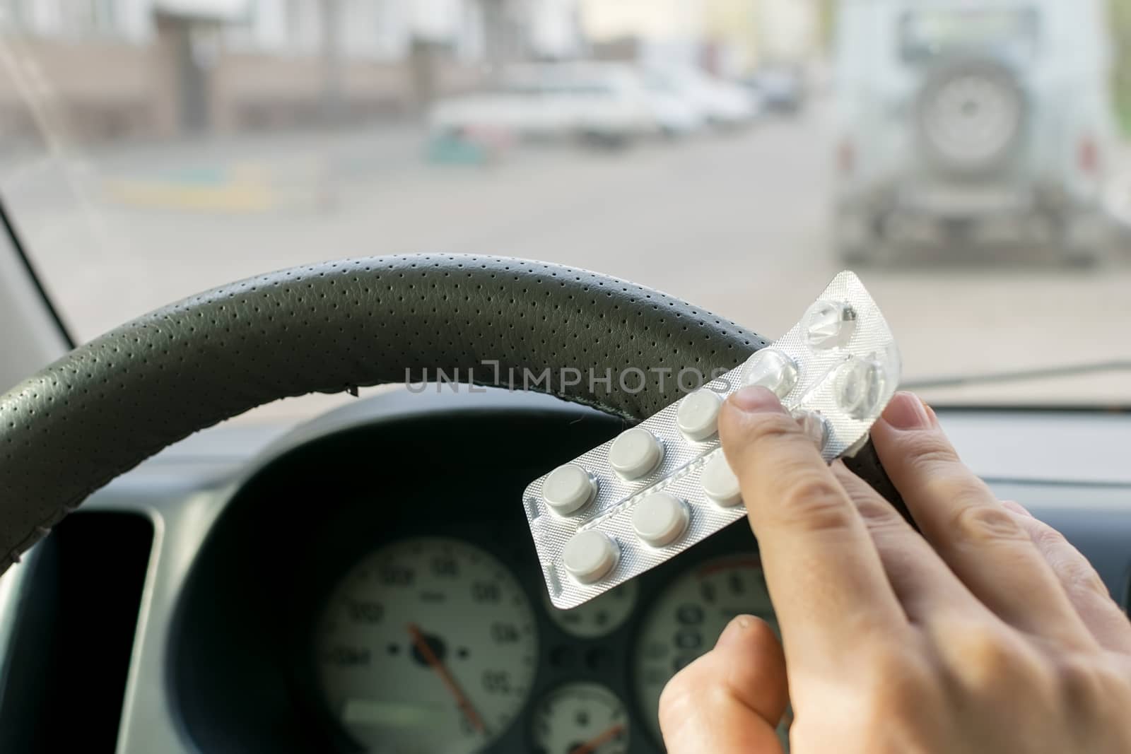 View of the driver's hand on the background of the steering wheel of the car, which holds a package of pills