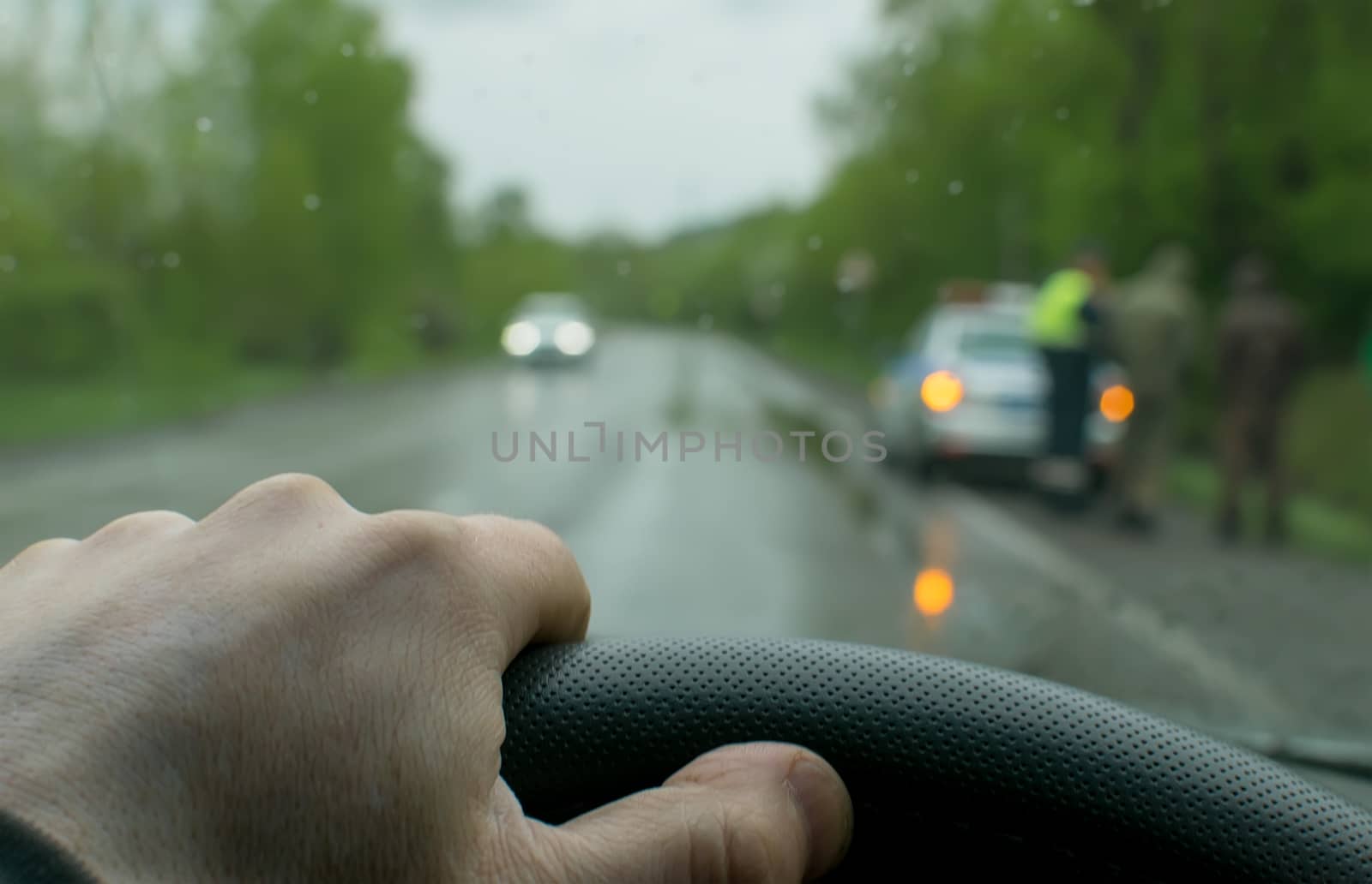 Rainy evening weather. Hand of the car driver close-up, against the background of people standing on the side of the road and a police car