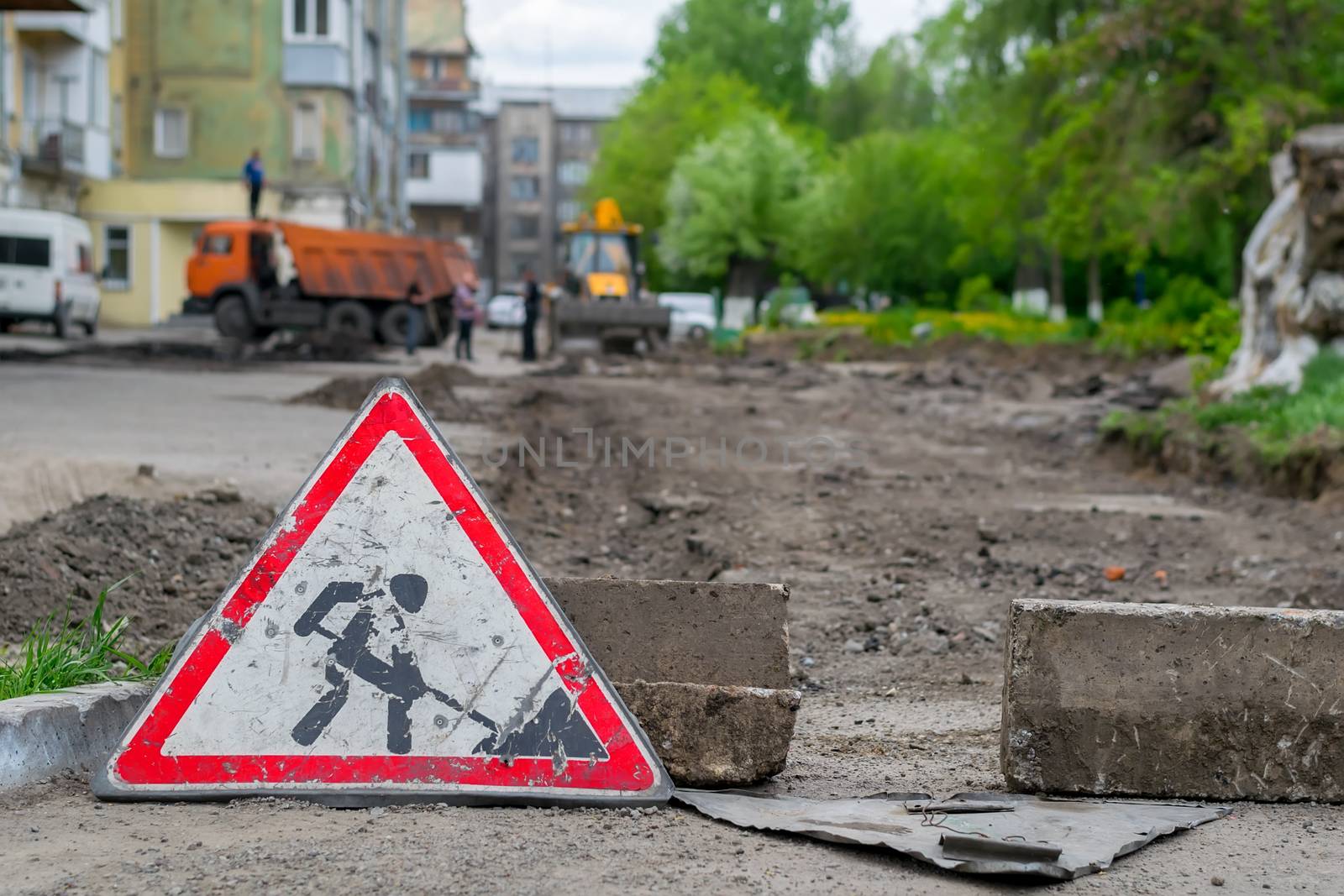 sign road repair stands on the background of the destroyed asphalt pavement in the courtyard of a multi-storey building, construction equipment and workers