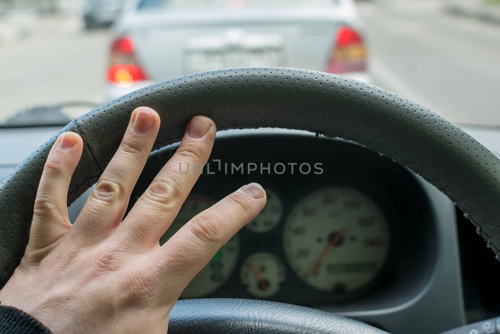 hand of the car driver on the steering wheel horn on the background of the car in front
