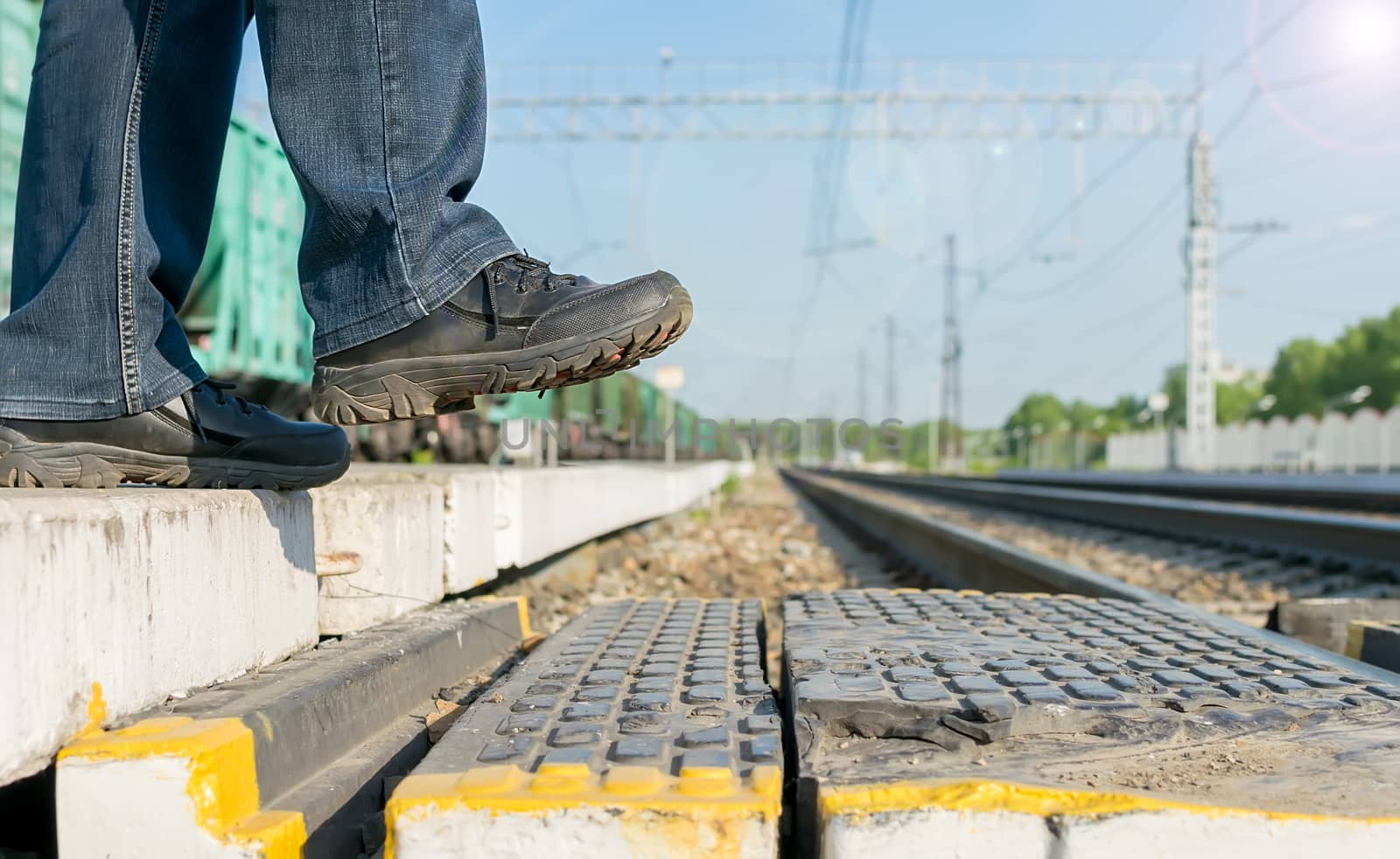 Pedestrian's feet step on a pedestrian crossing through the rails at the railway station on the background of freight cars