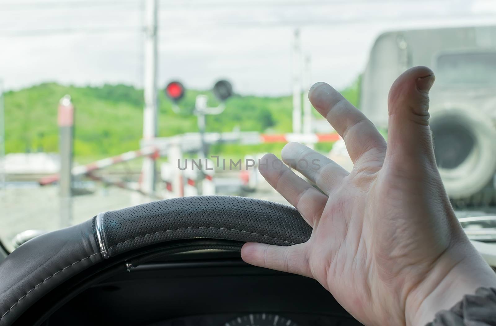 The hand of man inside the car. The car stopped in front of a closed barrier and a red traffic light before the railway crossing. Man outraged by the situation that did not have time to ride the move