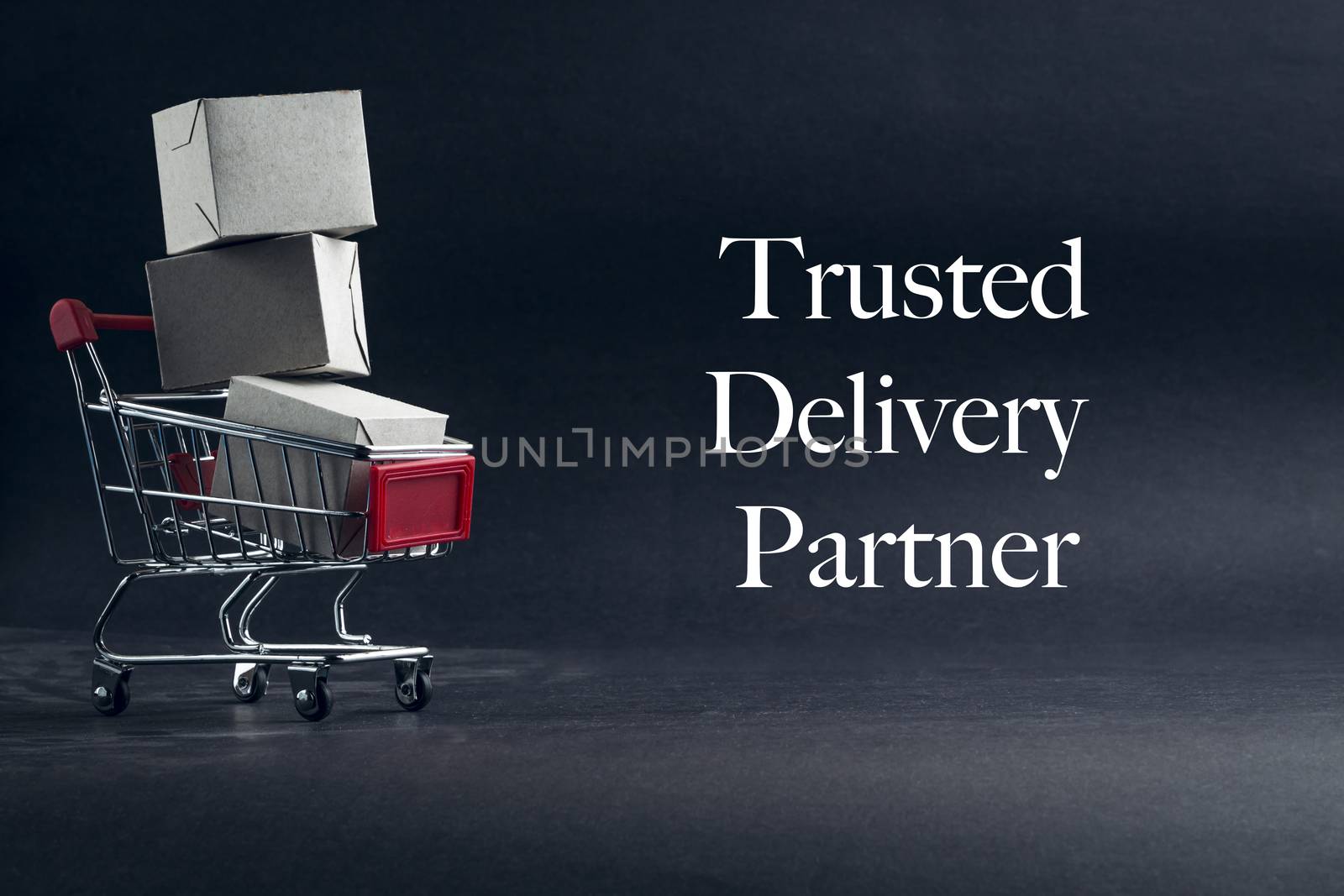 TRUSTED DELIVERY PARTNER text with shopping cart on dark background. Business, Copy space and online shopping concept. Selective focus