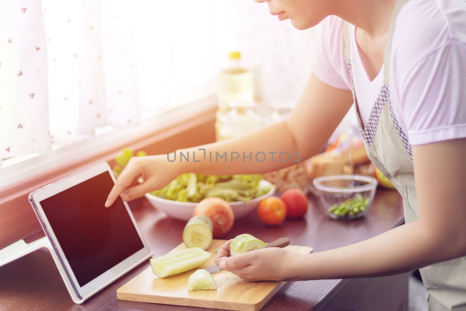 Asian woman use finger slide on tablet screen prepare ingredients for cooking follow cooking online video clip on website. cooking content on internet technology for modern lifestyle concept