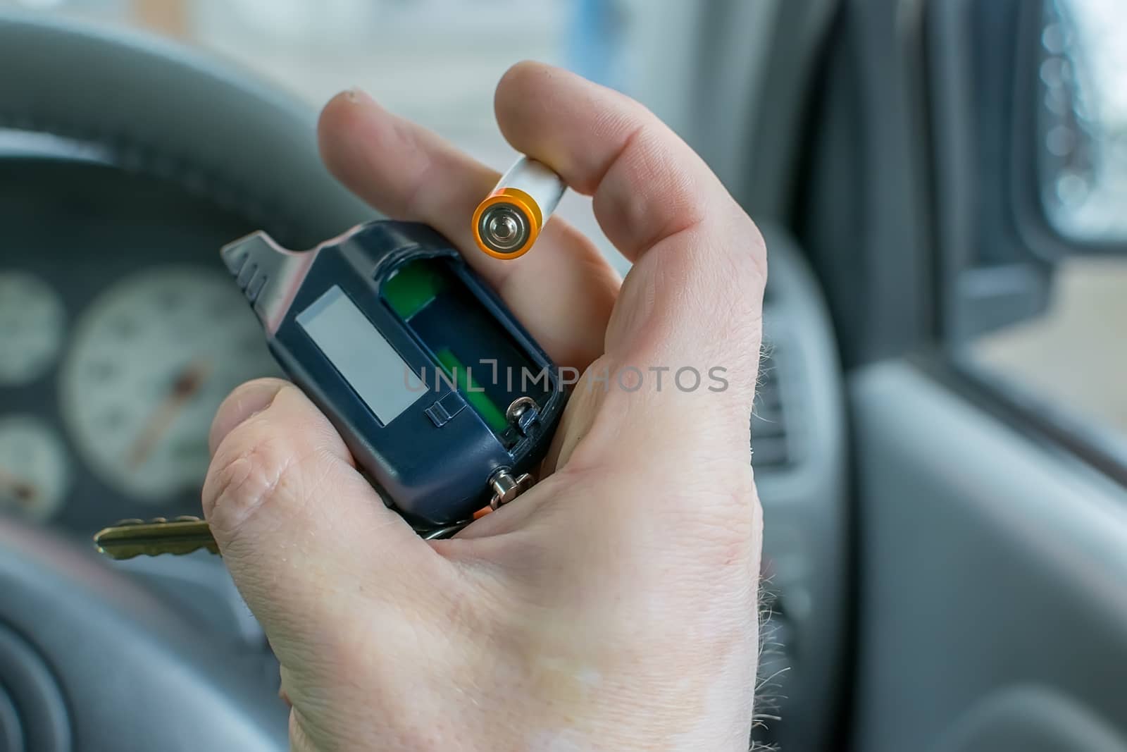 the hand of the person who is in the car holds the disassembled alarm keychain and a new battery for replacement