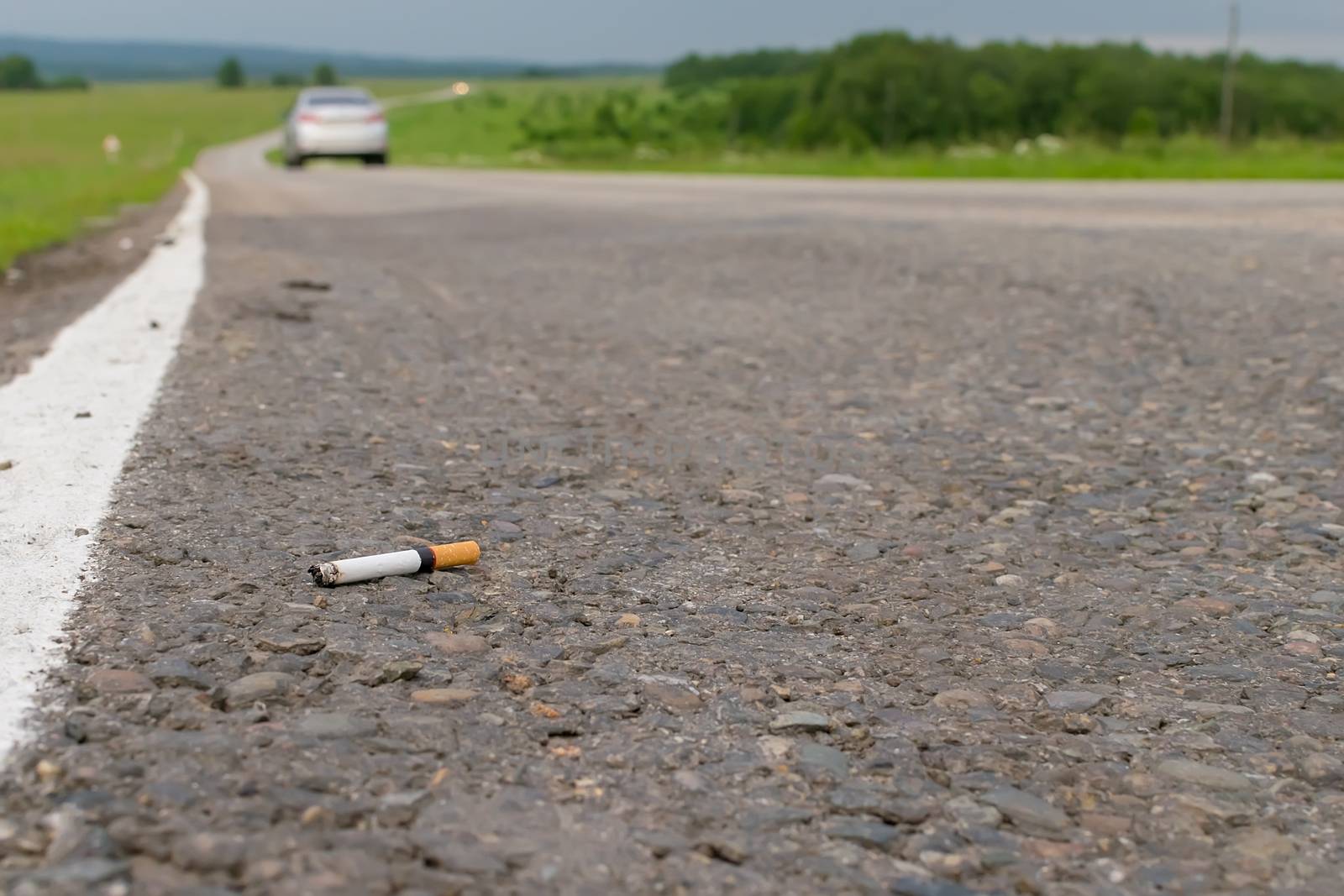 View of cigarette lying on the asphalt on a country road in the cloudy weather