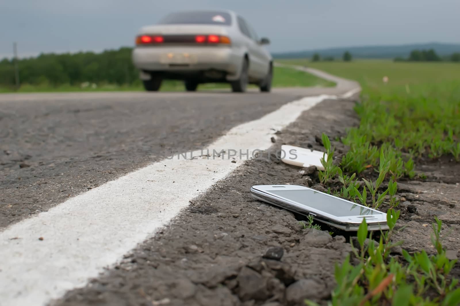 a discarded broken mobile phone is lying on the asphalt against the background of a passing car