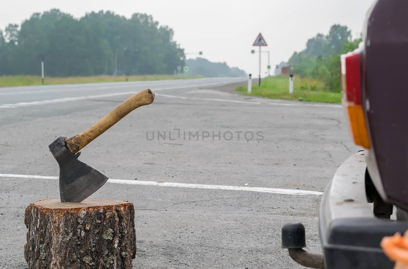 view of the ax, which is stick in a wooden chock on the background of a country road