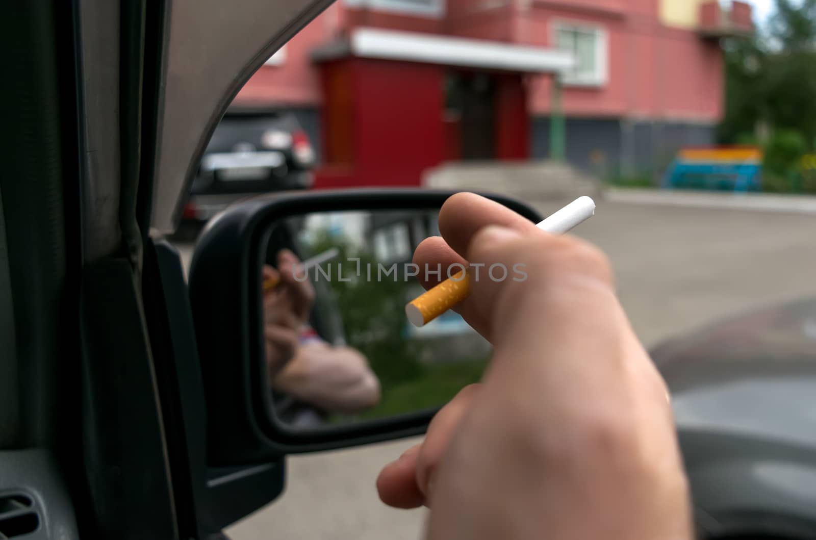 close-up of a cigarette in the hand of a man in the car, who watches the entrance door of the house