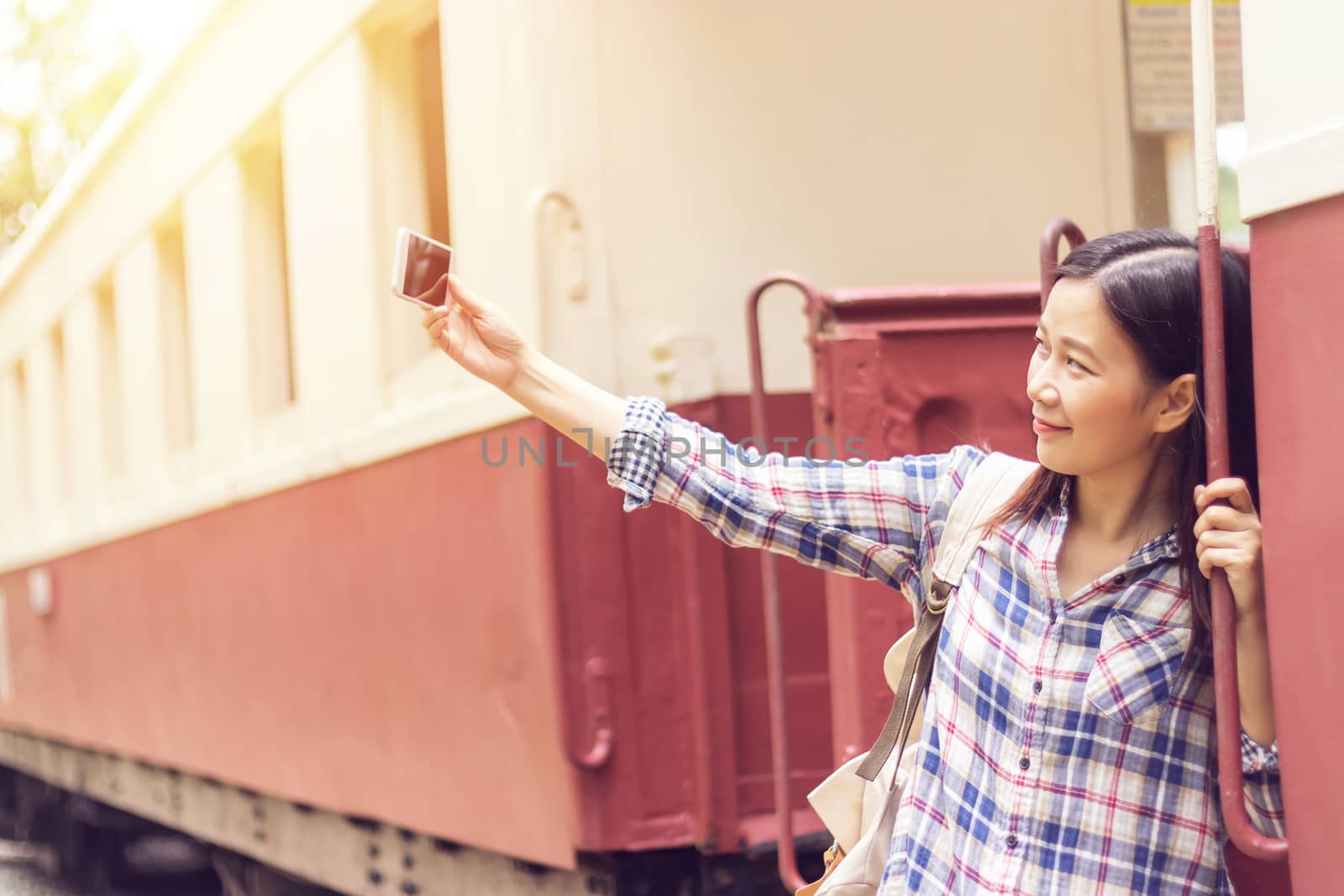 happy young Asian traveller woman taking selfie photo from mobile phone at train station while traveling by asiandelight