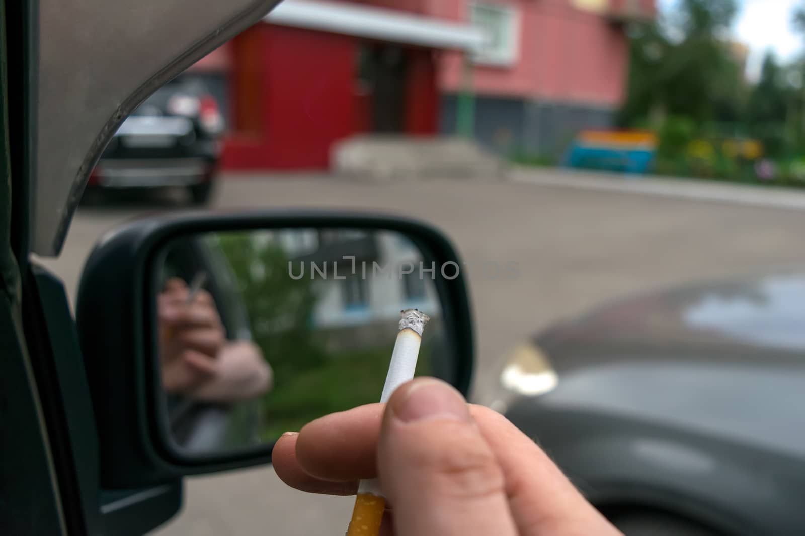 close-up of a cigarette in the hand of a man in the car, who watches the entrance door of the house