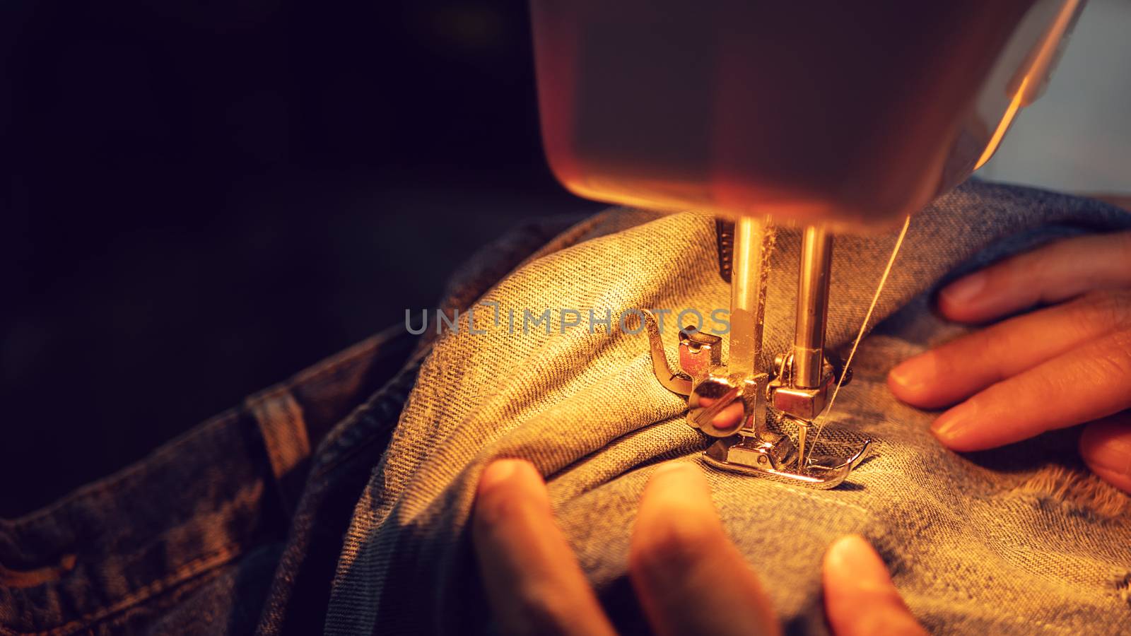 close up of a woman sewing blue denim jeans with a sewing machine