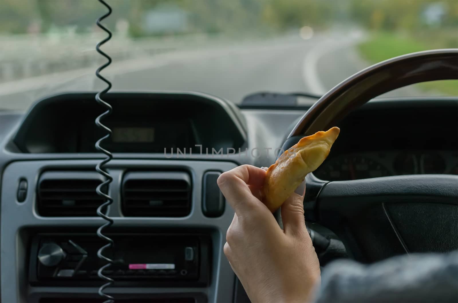 Closeup, of female hand holding a bun behind the wheel of the car in motion on highway