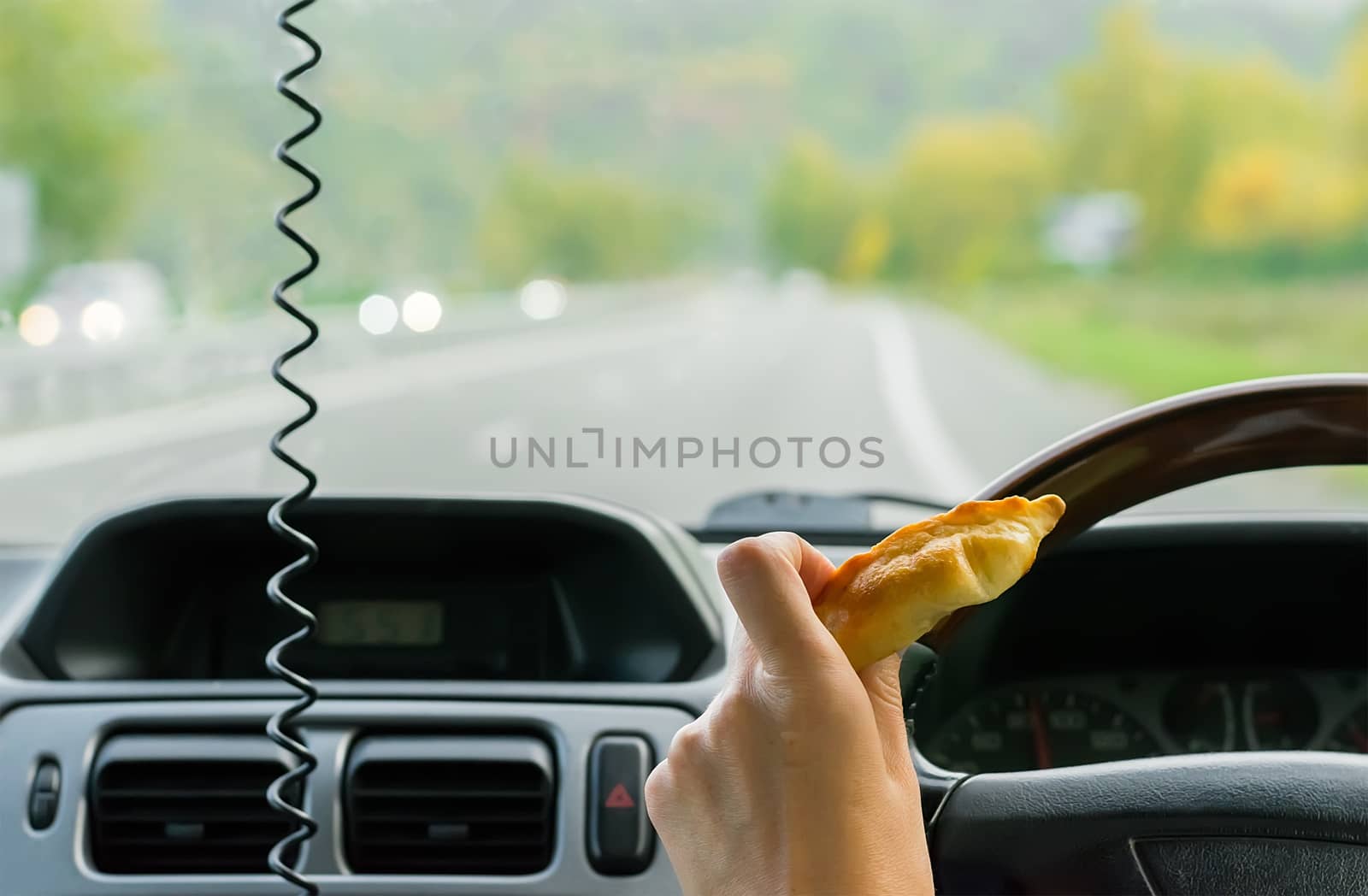 Closeup, of female hand holding a bun behind the wheel of the car in motion on highway