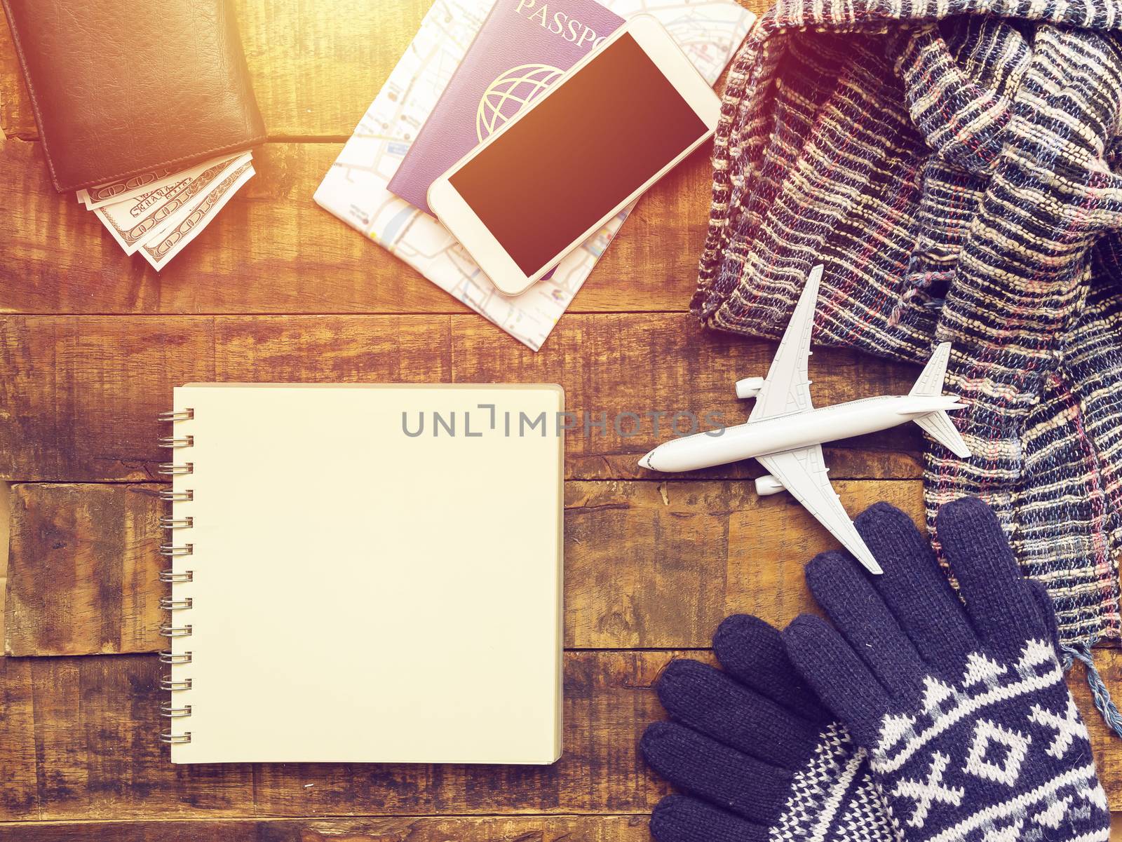 flat lay of passport ,mobile phone , plane model , scarf , gloves and traveler's accessories items on wooden background with blank paper for copy space. travel and vacation concept