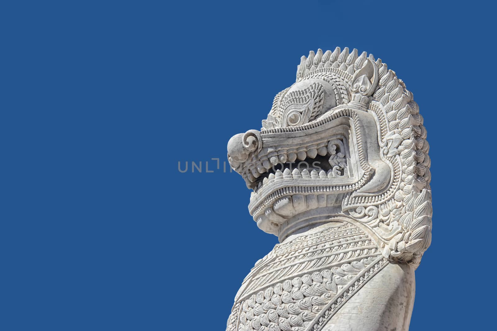 sculpture of ancient white stone singha statue isolated on blue sky background in front of temple in Bangkok, Thailand , Southeast Asia
