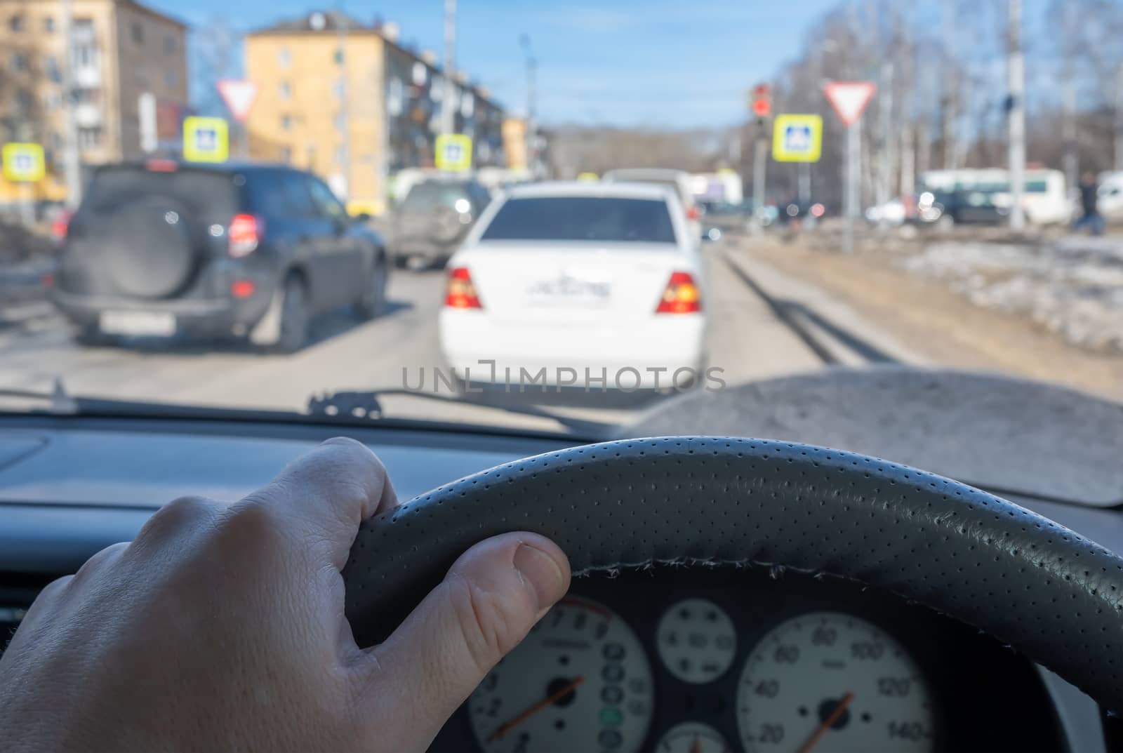 the driver hand on the steering wheel of a car against the background of a street with cars standing in a traffic jam at an intersection with a traffic light