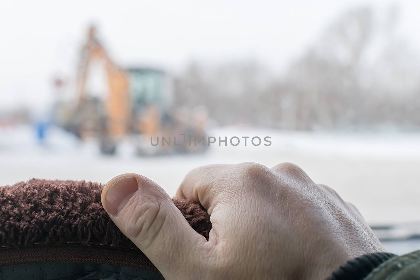 close up of the driver hand on the steering wheel of a car in winter on the background of a construction tractor