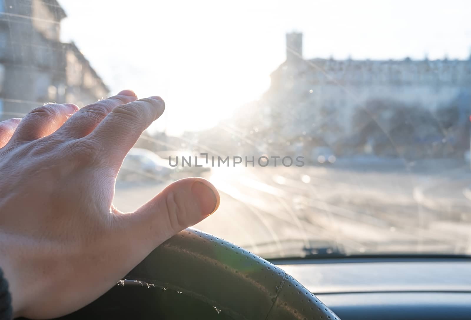 The hand of the driver of the car covers the sunlight, which blinds the person to see the road situation