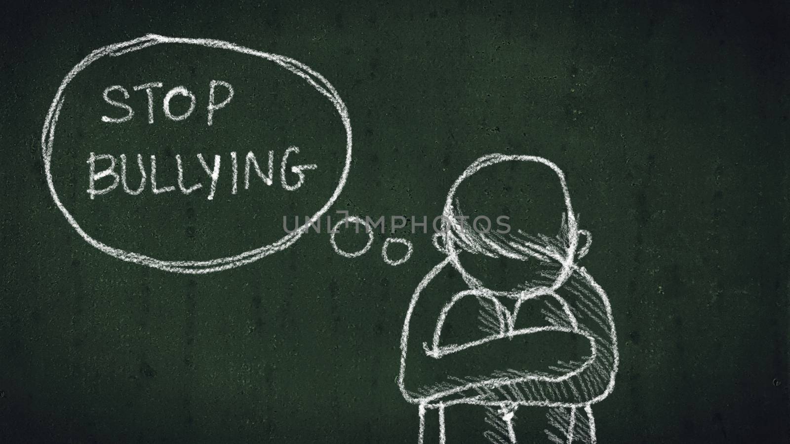 sad young boy sitting on the floor with text stop bullying written with chalk on chalkboard. social problems of humanity