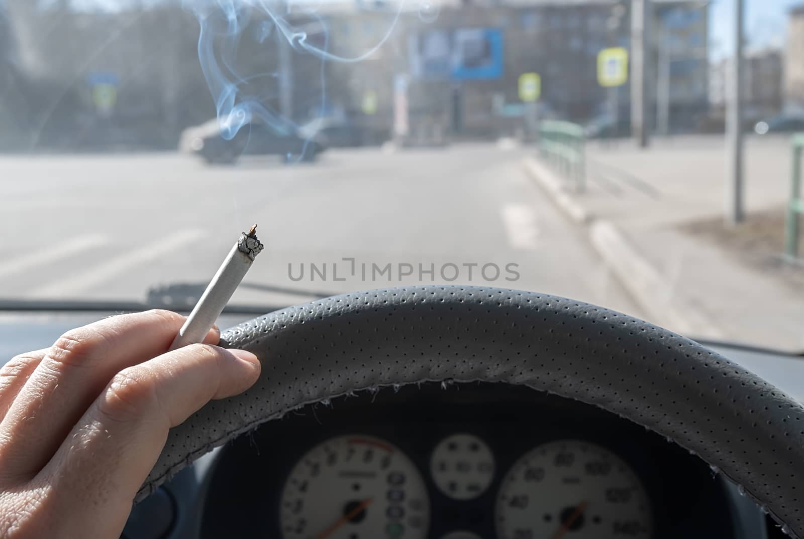 a Smoking cigarette in the hand of a Smoking car driver while driving through the city against the background of a car intersection and pedestrian crossing