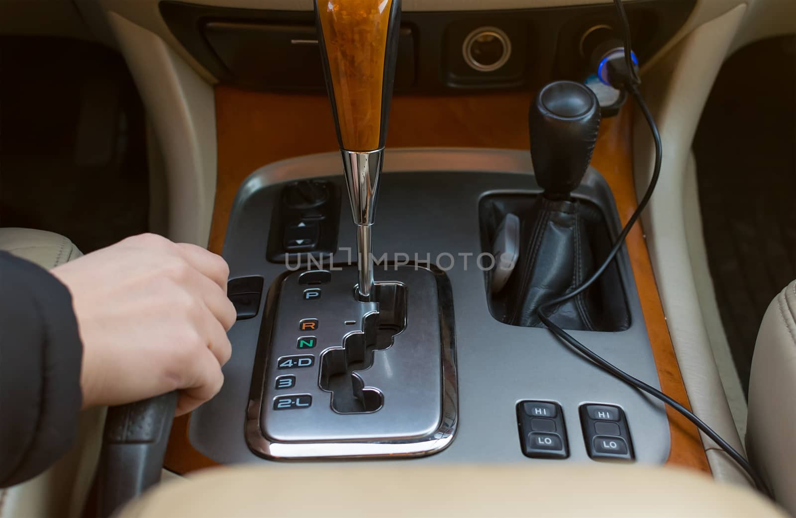 The hand of the driver of the car holding the brake lever, on the background of the automatic transmission controls, close-up view