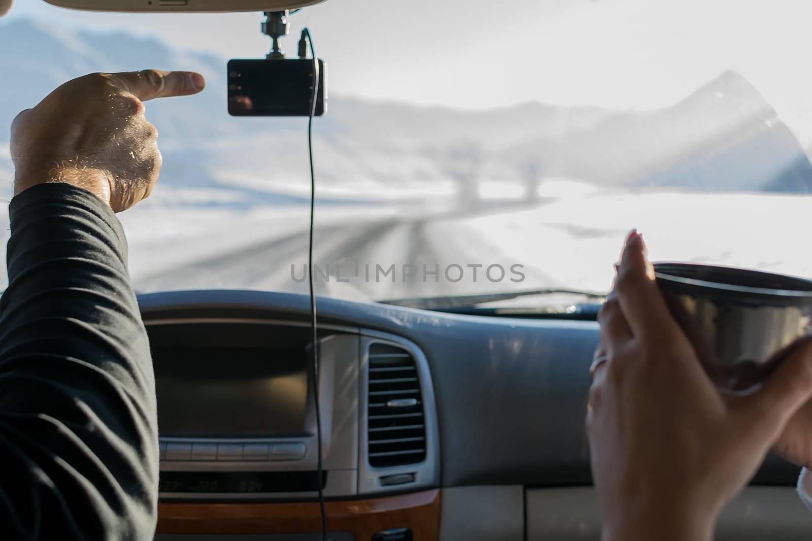 The hand of a man, the driver, shows the girl with a mug of tea, the direction of the road, in winter, in the snow-covered mountain area