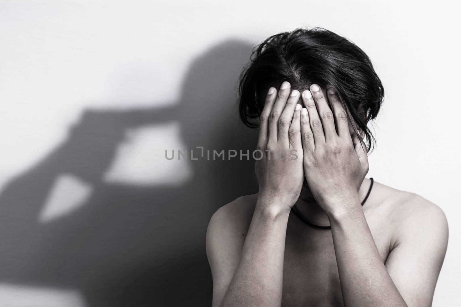 man with depression sitting head in hands with shadow of gun that was pointing his head, thinking to commit suicide. depression anxiety and bully victim problem concept by asiandelight