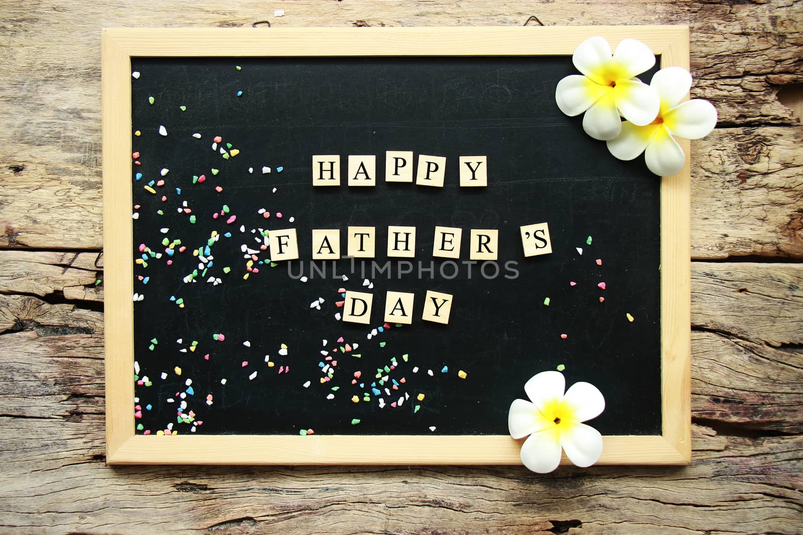 happy father's day word from wooden block place on black chalk board decorate with tropical flower on wooden background