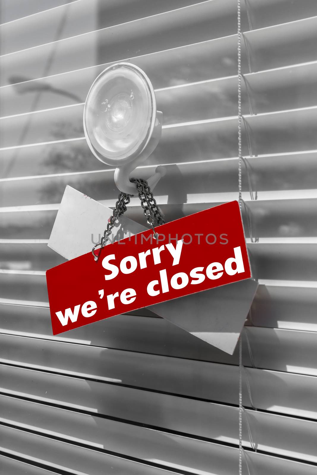 Sign saying "sorry we're closed" on a glass door with a white, closed venetian blind. It can be used for business concepts or backgrounds.
