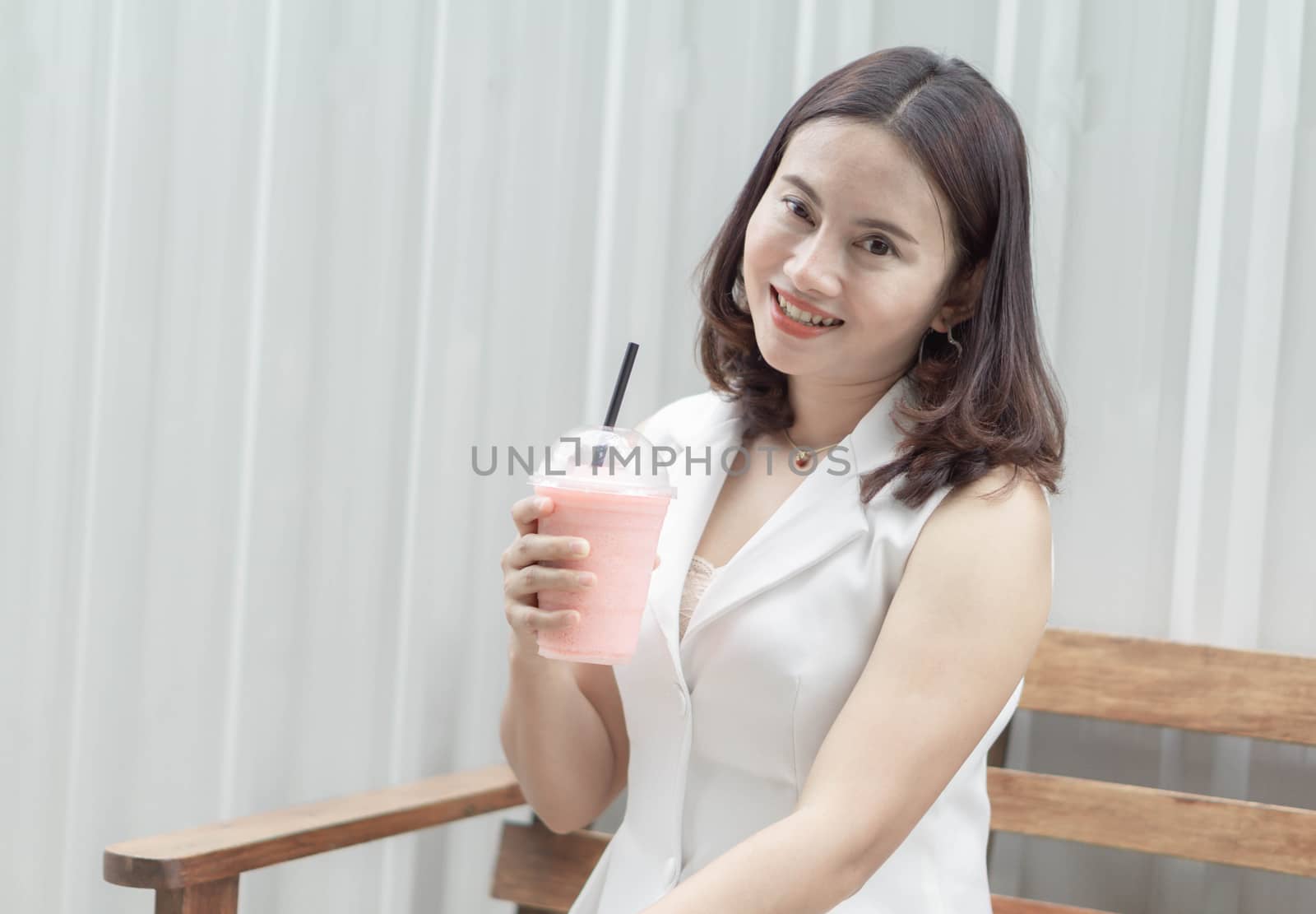 Closeup woman drinking strawberry smoothie and cake with green nature background, selective focus