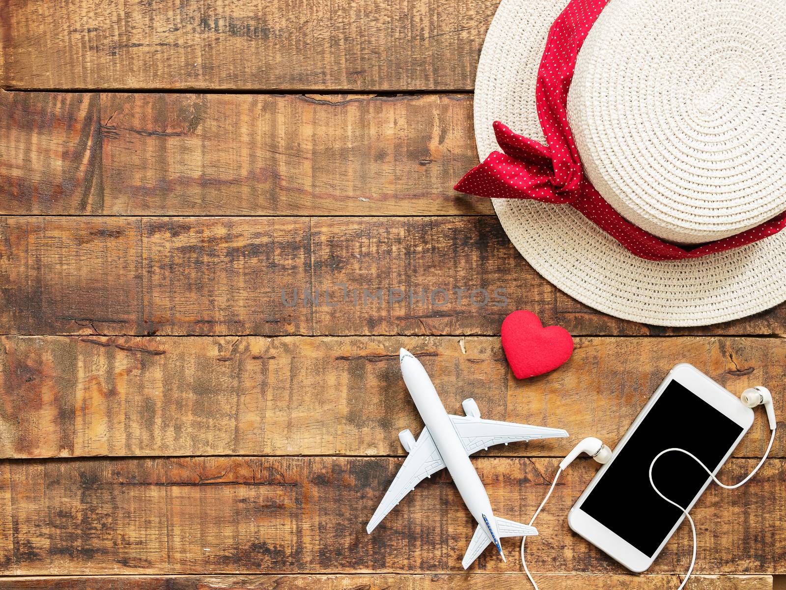 flat lay of plane model , red heart shape ,mobile ,earphone and woman hat as traveler's accessories items on wooden background with copy space inside colorful bead frame. travel and vacation for girl